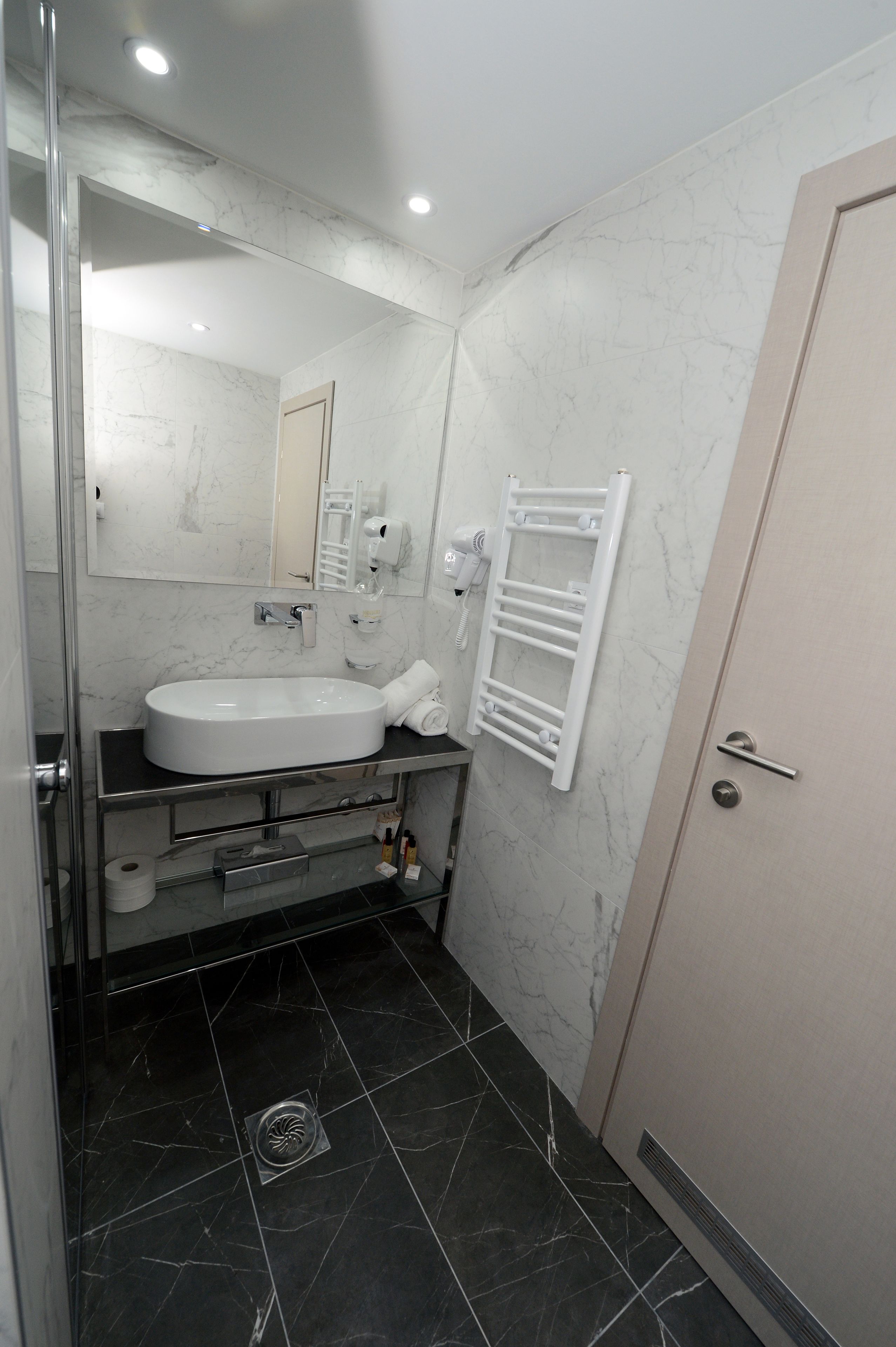Un baño moderno con un lavamanos grande, un espejo, un perchero para toallas y una zona de ducha.