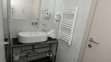 Un baño moderno con un lavamanos grande, un espejo, un perchero para toallas y una zona de ducha.