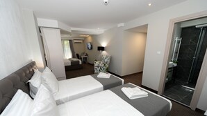 A hotel room with two beds, a sitting area with a chair, a small table, and a shower area. - Hotel Alexandar II (Skopje)