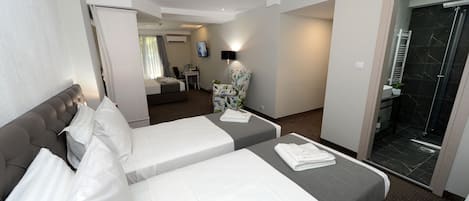 Une chambre d’hôtel avec deux lits, un coin salon comprenant une chaise et une petite table, ainsi qu’un espace douche.