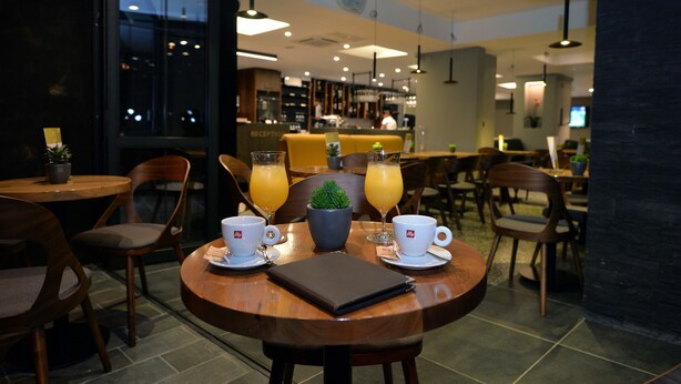 A restaurant with round tables, chairs, and a reception area in the background. - Hotel Alexandar II (Skopje)