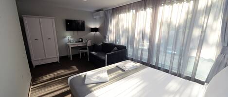 A hotel room with a bed, a desk, a chair, a wardrobe, and a large window with curtains.