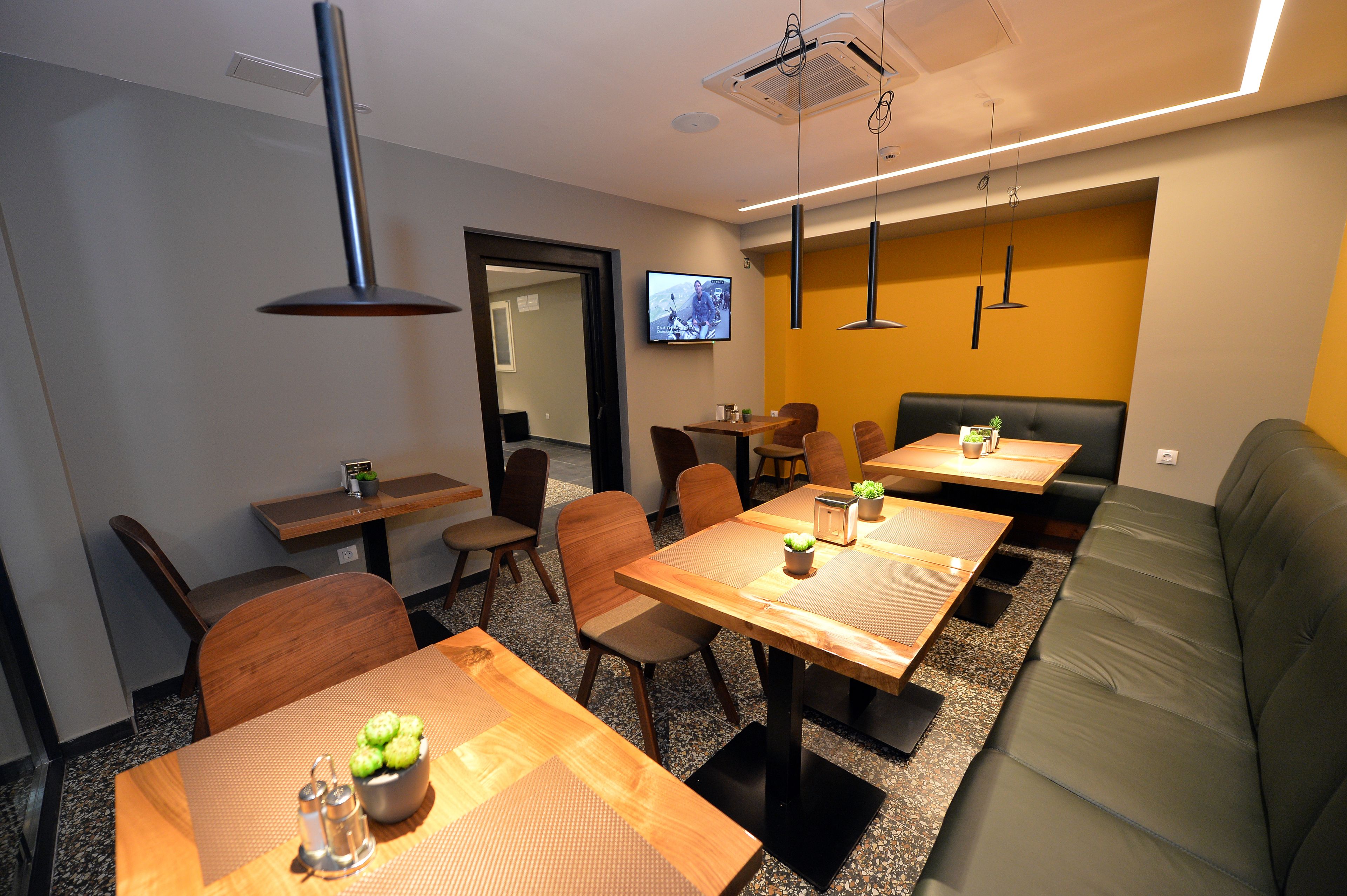 A modern dining area with wooden tables and chairs, a sofa, and a television mounted on the wall.