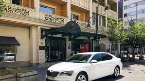 A white car parked in front of a building with a sign reading "ALEXANDAR SQUARE" and "HOTEL". - Hotel Alexandar II (Skopje)