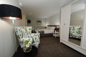 Habitación de hotel con cama, una silla, una mesita, una lámpara y un espejo.