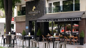 An outdoor café area with tables and chairs, a sign for 'BISTRO CAFÉ', and a building with a sign for 'ALEXANDAR II HOTEL'. - Hotel Alexandar II (Skopje)