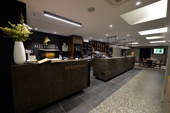 A reception area with a reception desk labeled "RECEPTION," a wall-mounted TV, and a bar area with shelves of glasses and bottles.