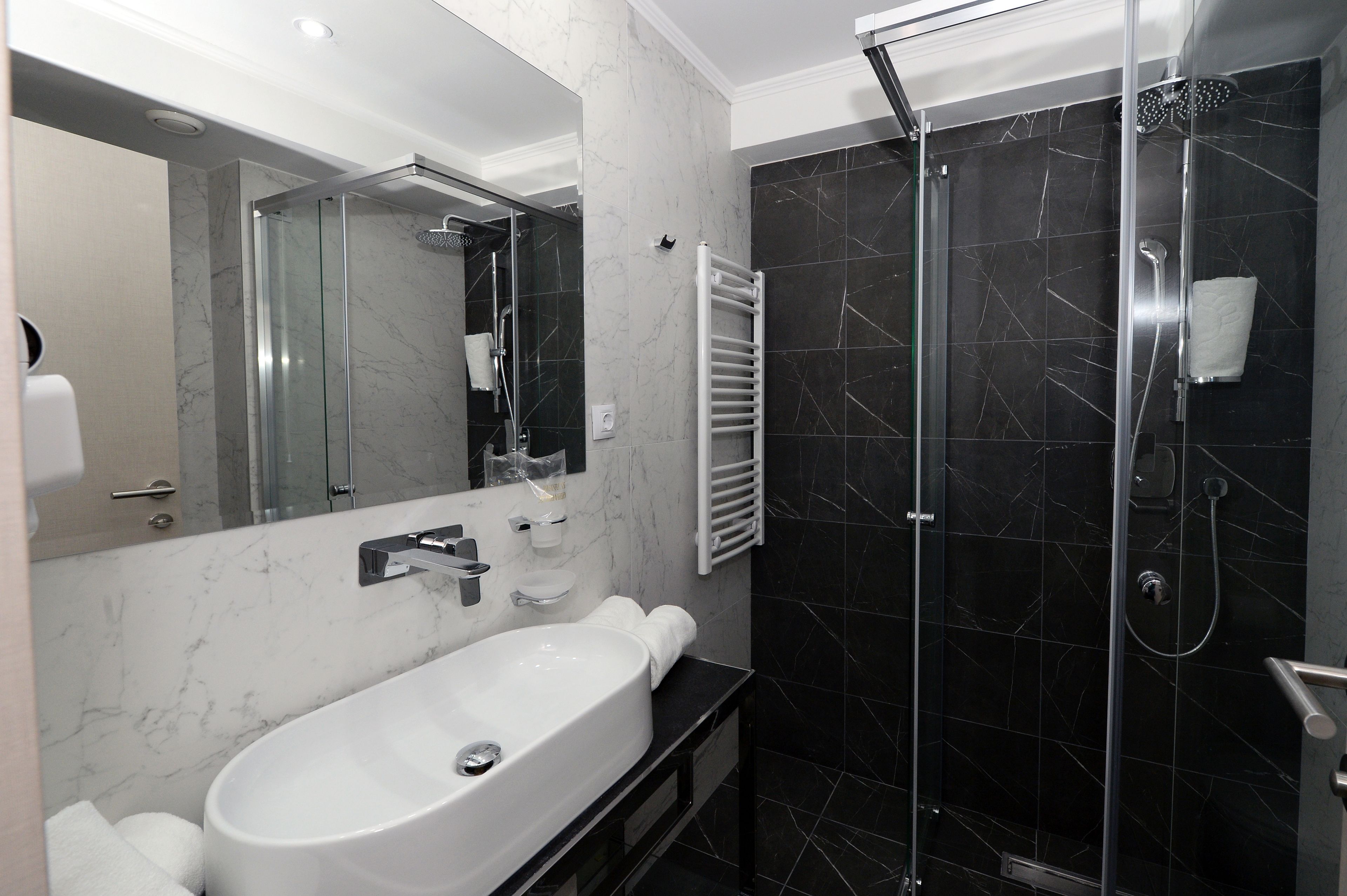 A modern bathroom with a large white sink, a glass-enclosed shower, and dark marble walls.