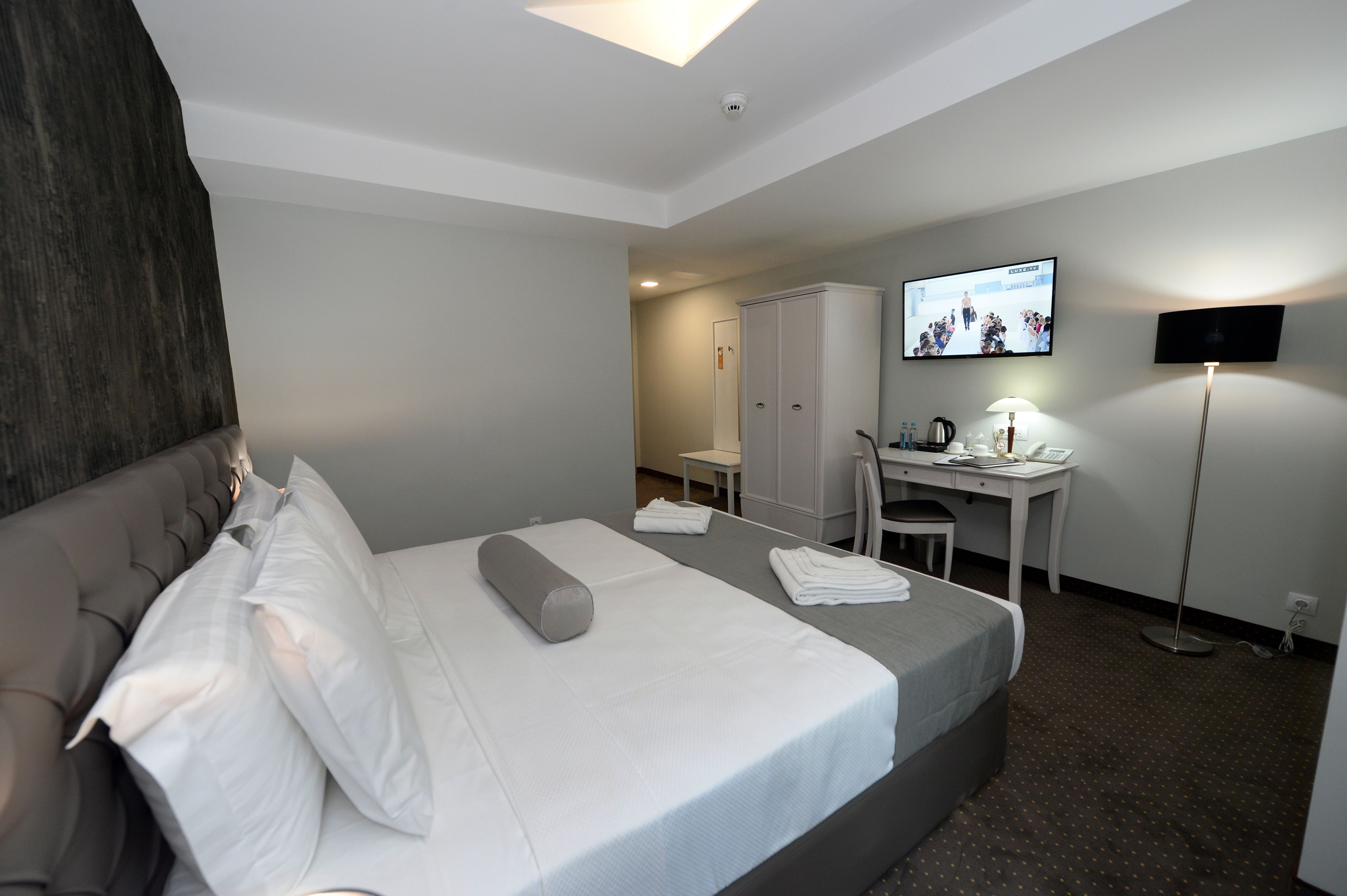 Quarto de hotel com cama, escrivaninha, cadeira, televisão e guarda-roupa.
