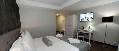 Quarto de hotel com cama, escrivaninha, cadeira, televisão e guarda-roupa.