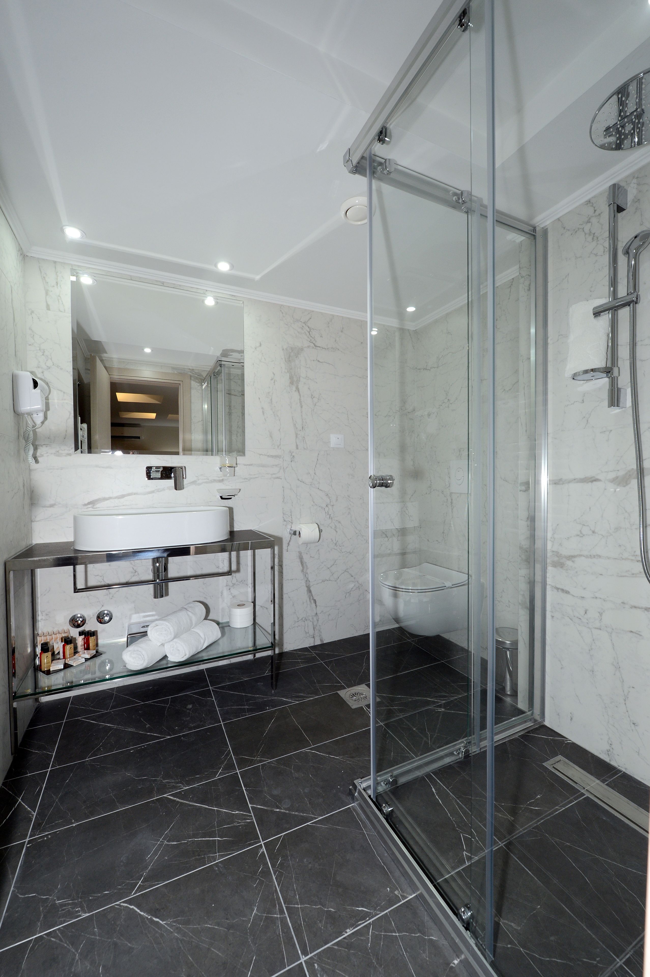 Een moderne badkamer met een douche met glazen wand, een witte wastafel en een vloer van marmer.