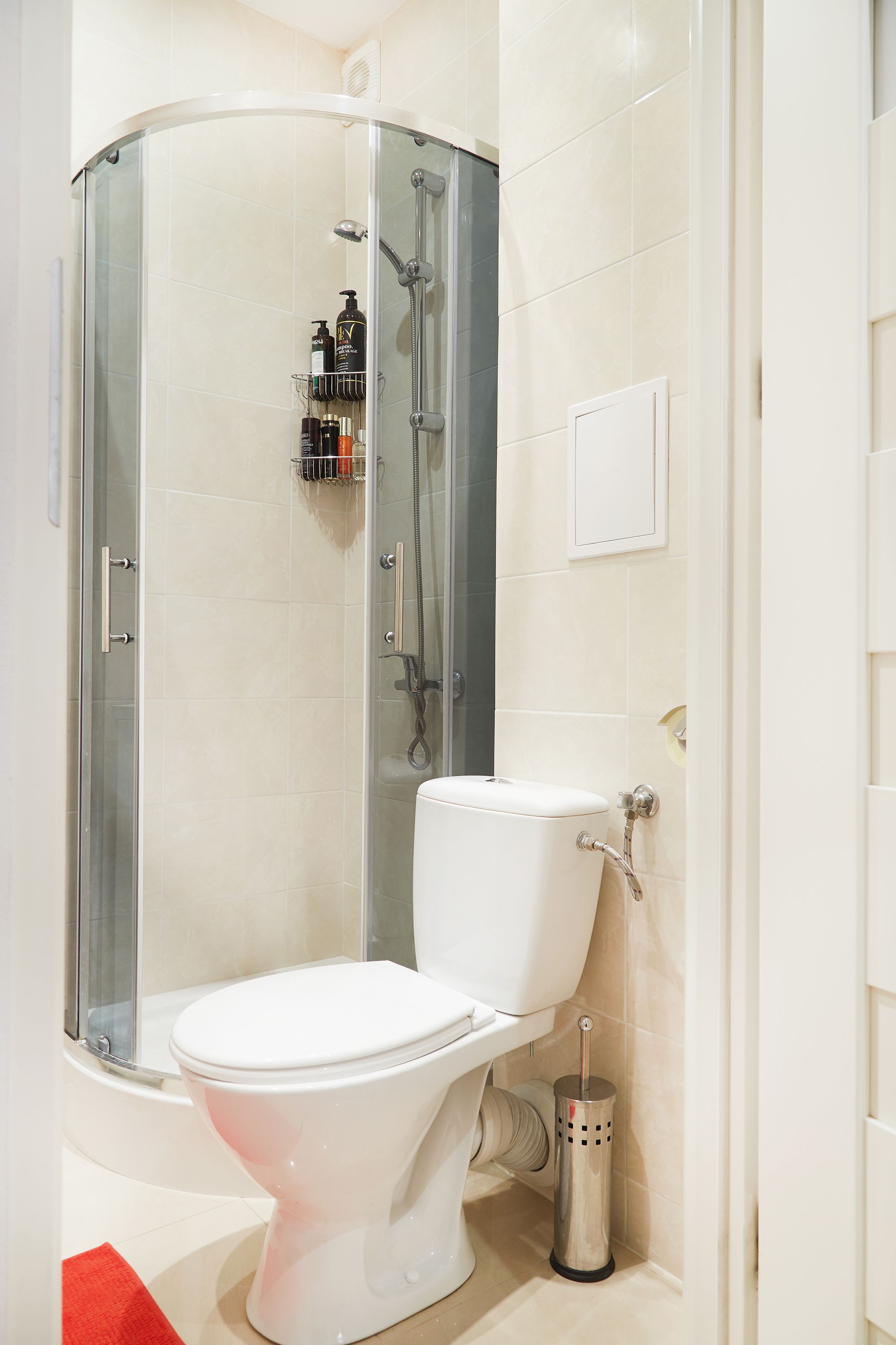 Une salle de bain moderne avec une douche à parois de verre, des toilettes blanches et une petite étagère contenant des articles de toilette.