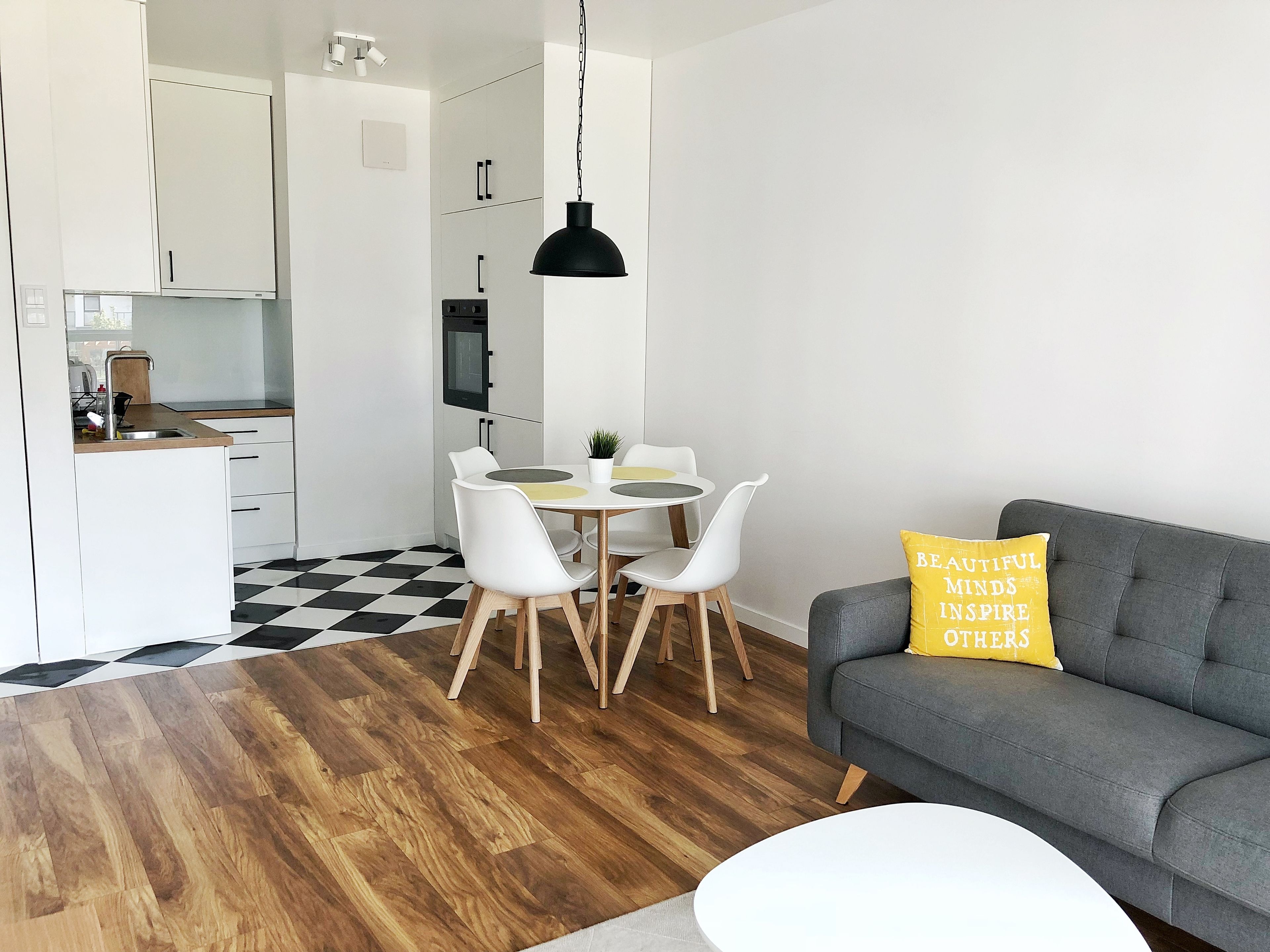 A modern living room with a grey sofa, a round white coffee table, and a yellow pillow with text.