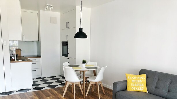 A modern living room with a grey sofa, a round white coffee table, and a yellow pillow with text.
