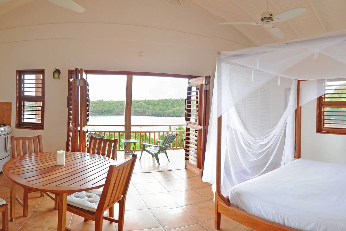 Een slaapkamer met hemelbed, een balkon met uitzicht op het water, en een keuken met een koelkast en magnetron.