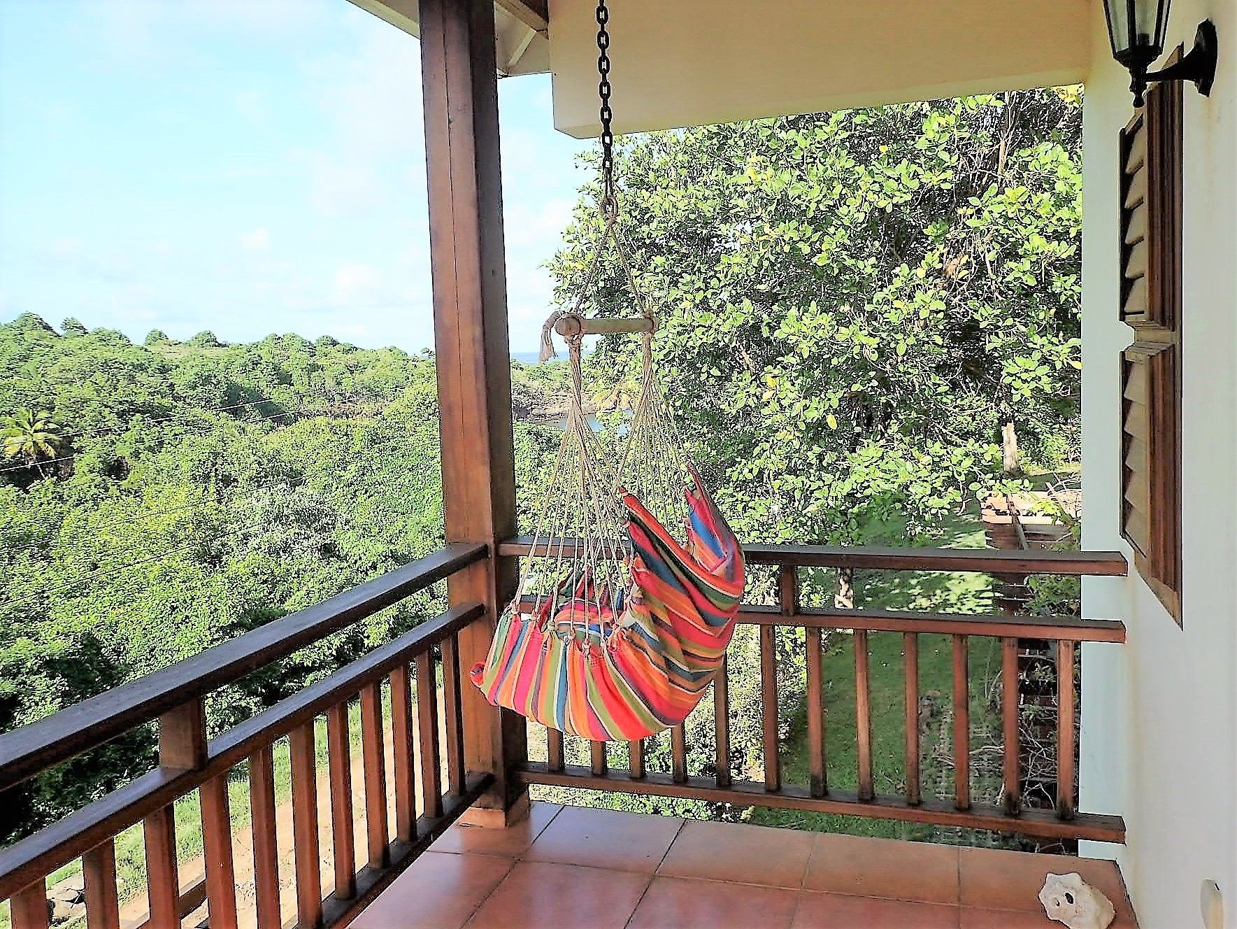 Un balcon doté d’un hamac, d’une balustrade en bois et offrant une vue sur une végétation luxuriante.