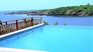 Piscina com deck de madeira e vista para o oceano.