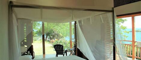 A bedroom with a bed, a ceiling fan, and a view of a garden and water body.