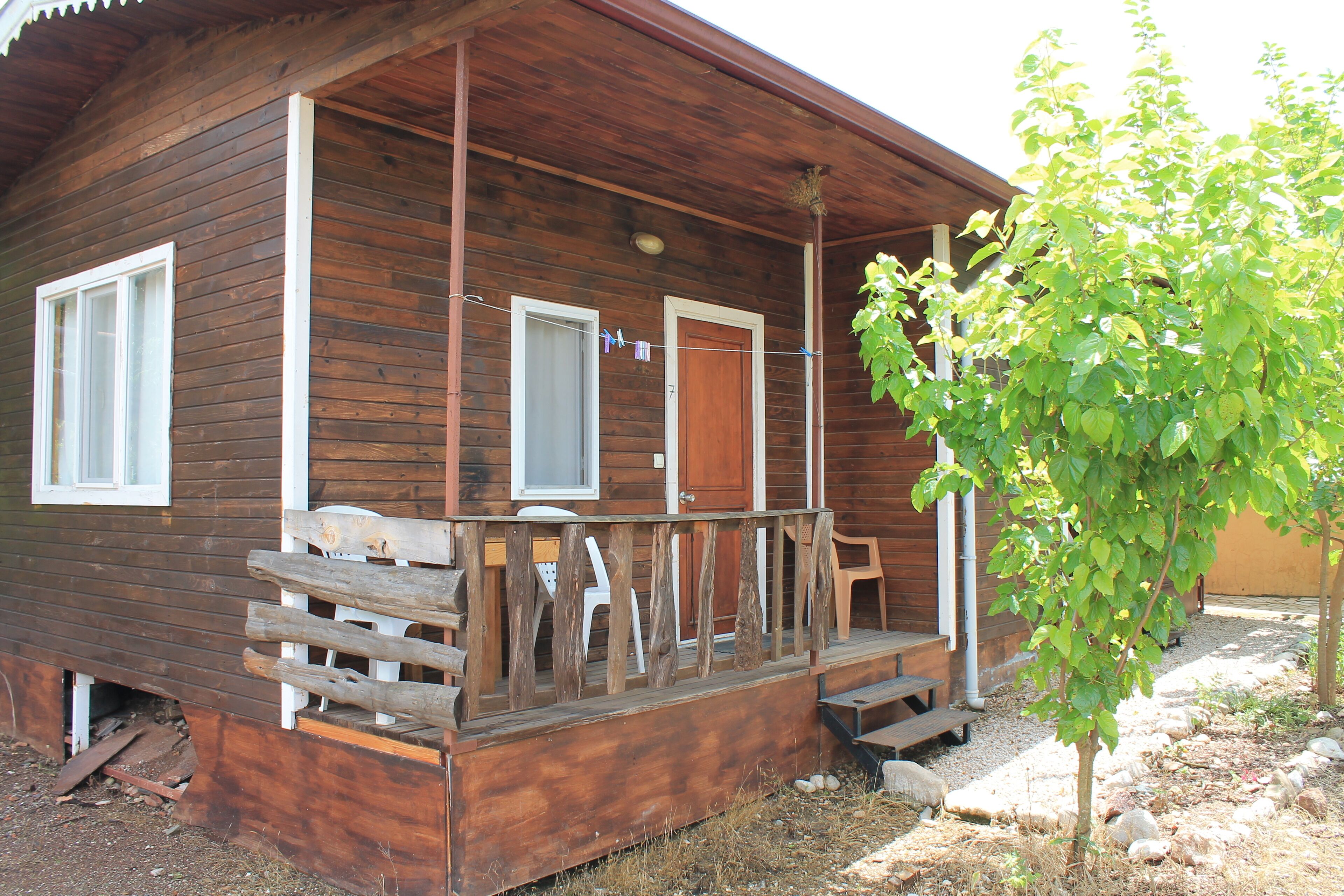 A wooden cabin with a porch, two windows, and a door.