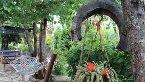 Una hamaca, un macetero colgante con cactus y flores, y una estructura de madera rústica.