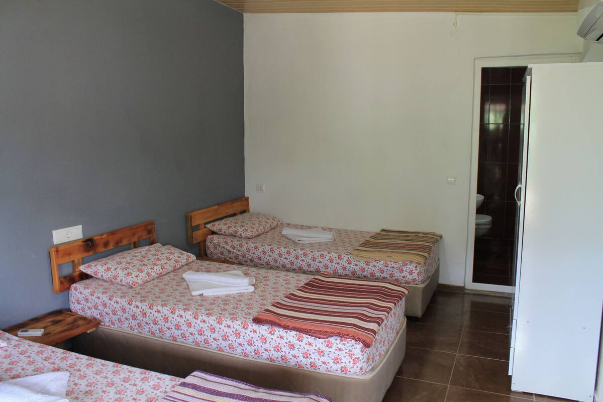 A room with three beds, each with floral bedding and striped blankets. There is a wooden headboard on the left bed, and a white door on the right.