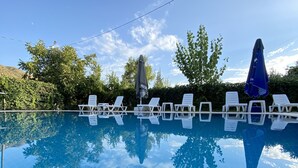 Piscina azul cristalina con sillas de descanso blancas y sombrillas, rodeada de follaje y árboles.