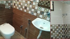 A bathroom with a toilet, sink, and shower. The walls are tiled with a floral pattern. - Hotel Jhanvi Palace (New Delhi)