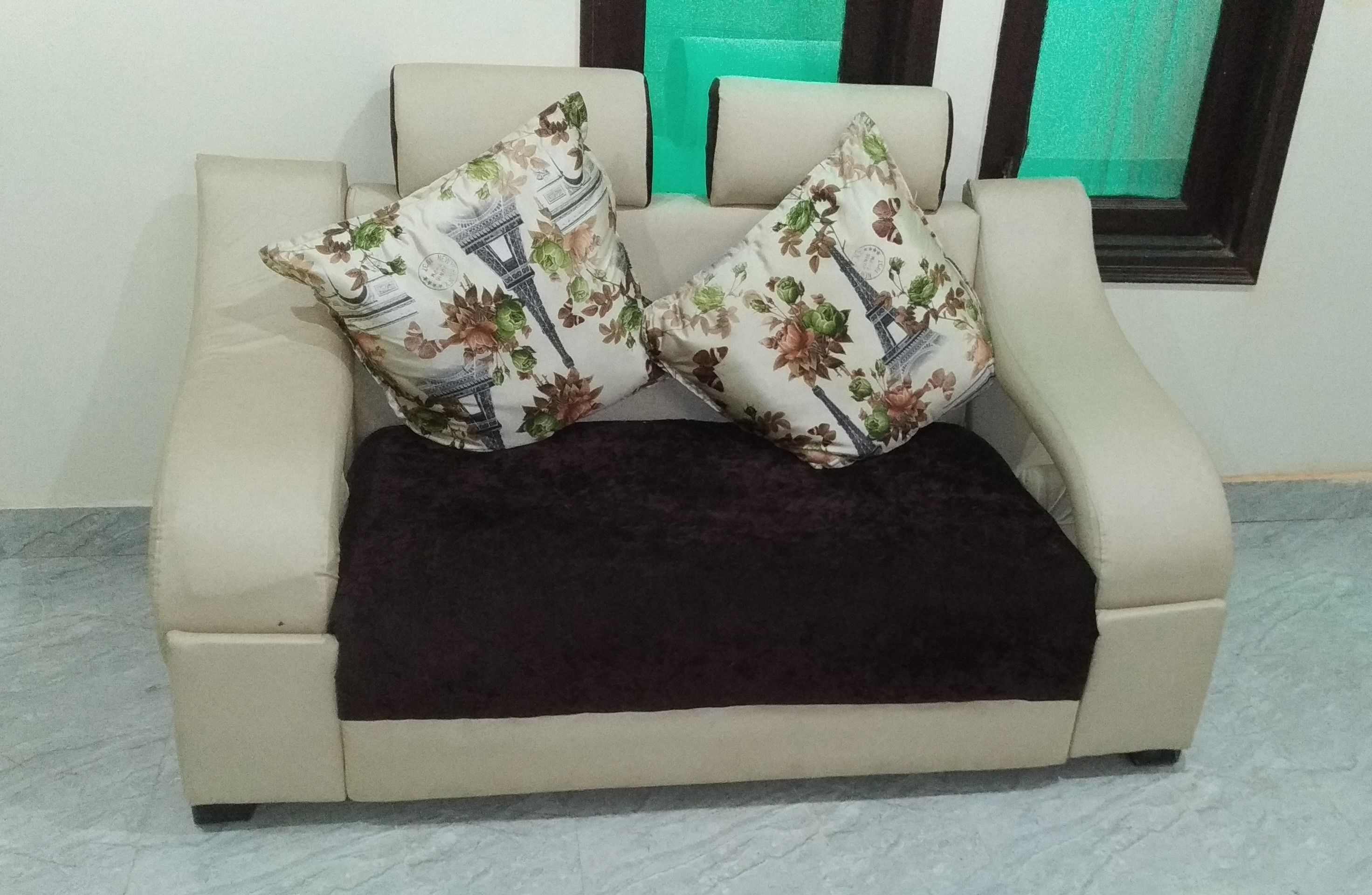 A beige sofa with two floral-patterned pillows and a dark throw blanket.