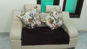 A beige sofa with two floral-patterned pillows and a dark throw blanket. - Hotel Jhanvi Palace (New Delhi)