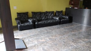 A room with a black sofa with floral patterns, a tiled floor, and a yellow wall. - Hotel Jhanvi Palace (New Delhi)