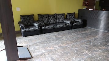A room with a black sofa with floral patterns, a tiled floor, and a yellow wall.