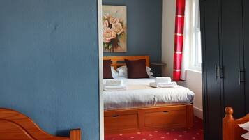 Ein Schlafzimmer mit Bett, Holz-Kopfteil, rotem Teppich, dunklem Kleiderschrank und einem Blumenbild an der Wand.
