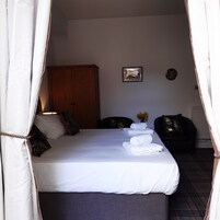 Una cama bien hecha con sábanas blancas y toallas enrolladas, un armario de madera, un cuadro en la pared y un jarrón con flores.