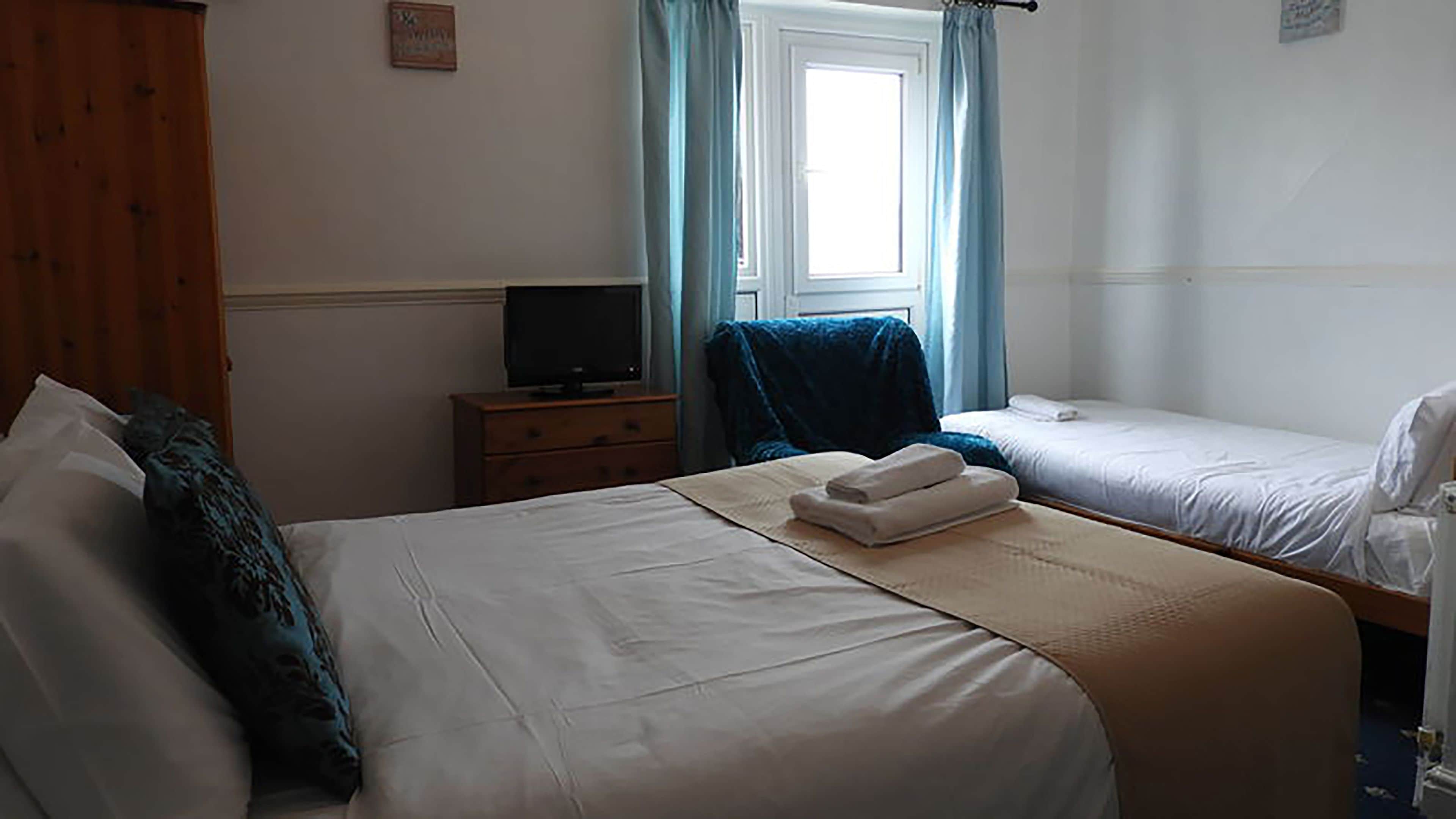 A hotel room with two beds, a TV on a wooden dresser, and a window with curtains.
