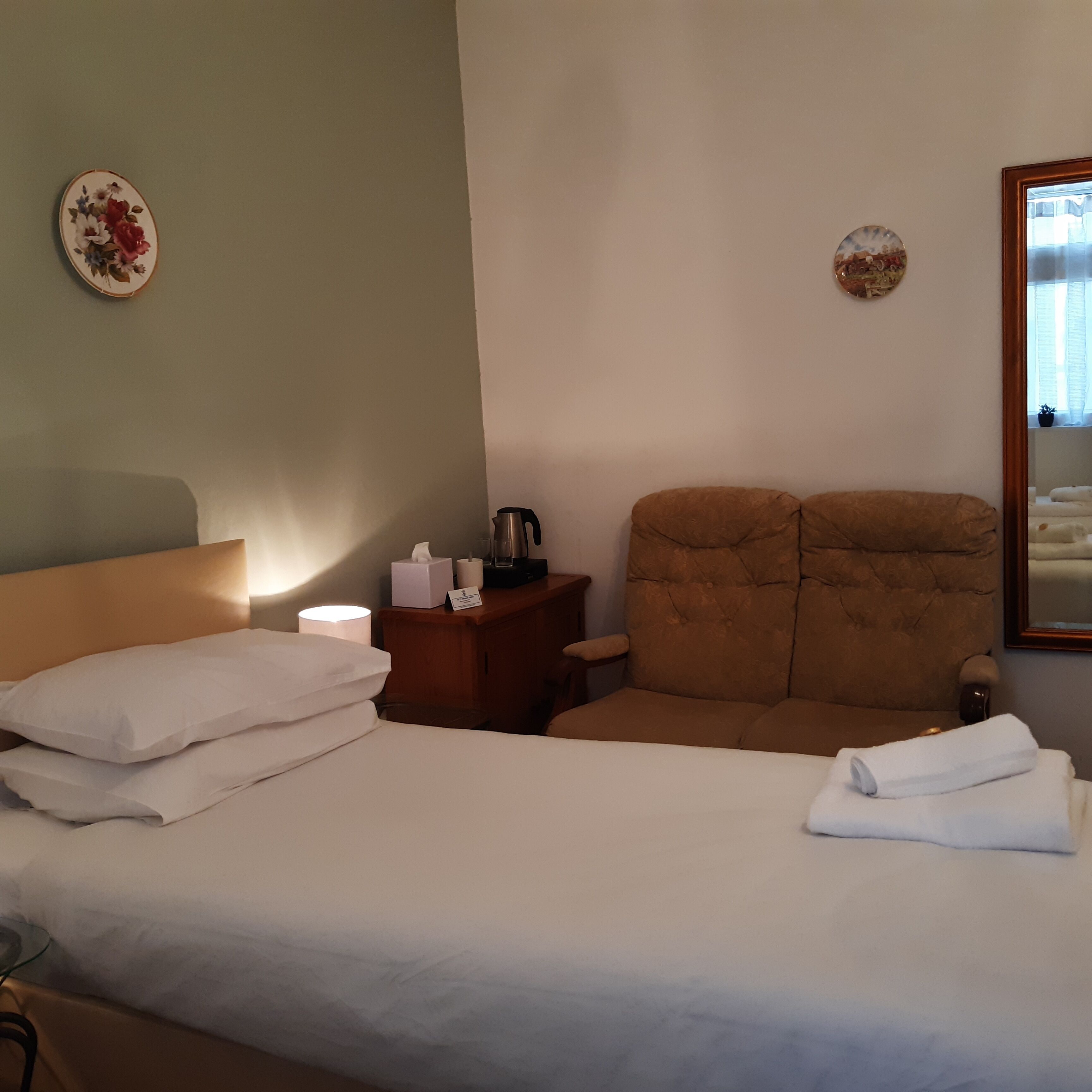 A hotel room with a bed, a chair, a nightstand, and a bedside table.