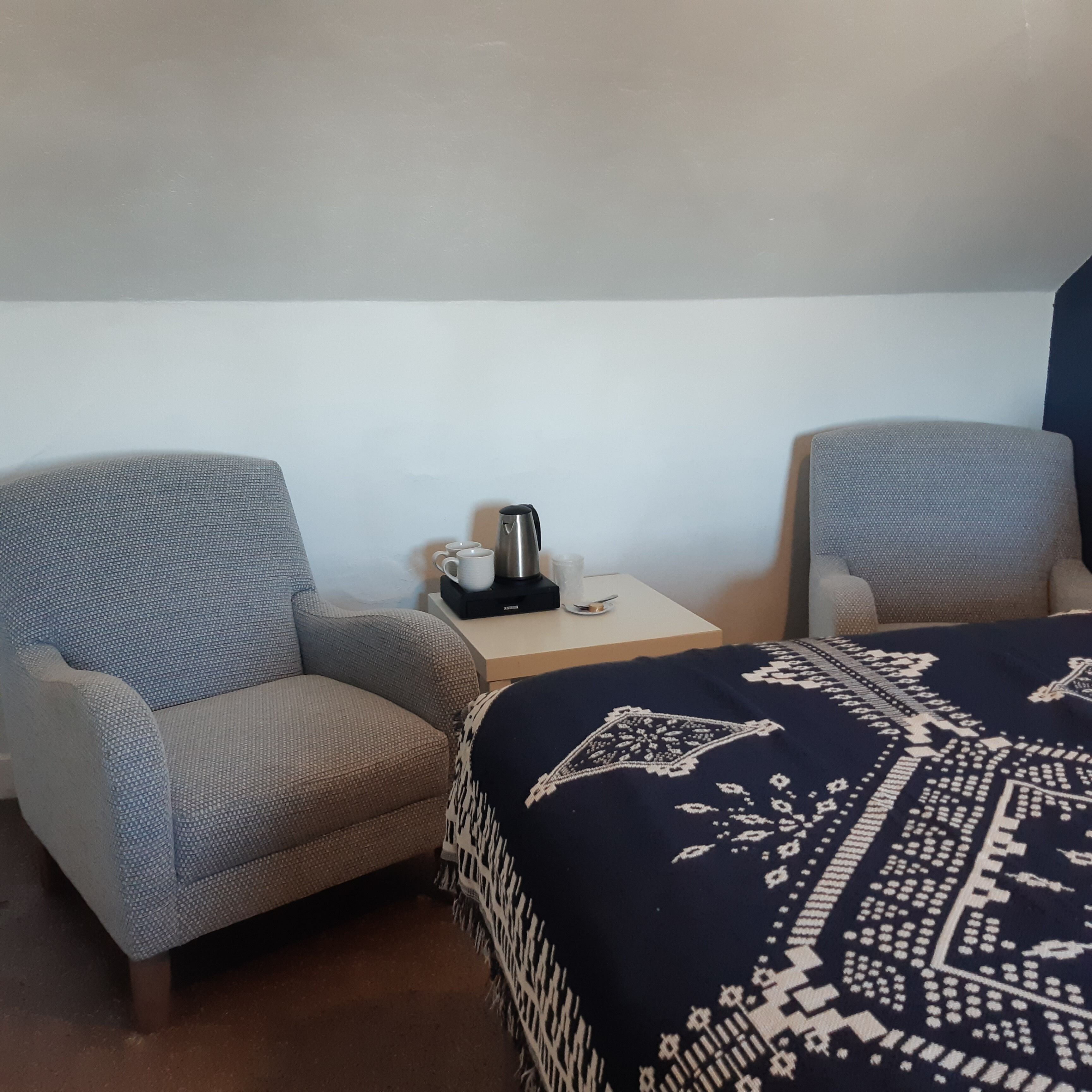 Een hotelkamer met twee fauteuils, een tafeltje met een koffiezetapparaat en een bed met een gestreept sprei.