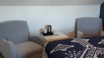 Een hotelkamer met twee fauteuils, een tafeltje met een koffiezetapparaat en een bed met een gestreept sprei.