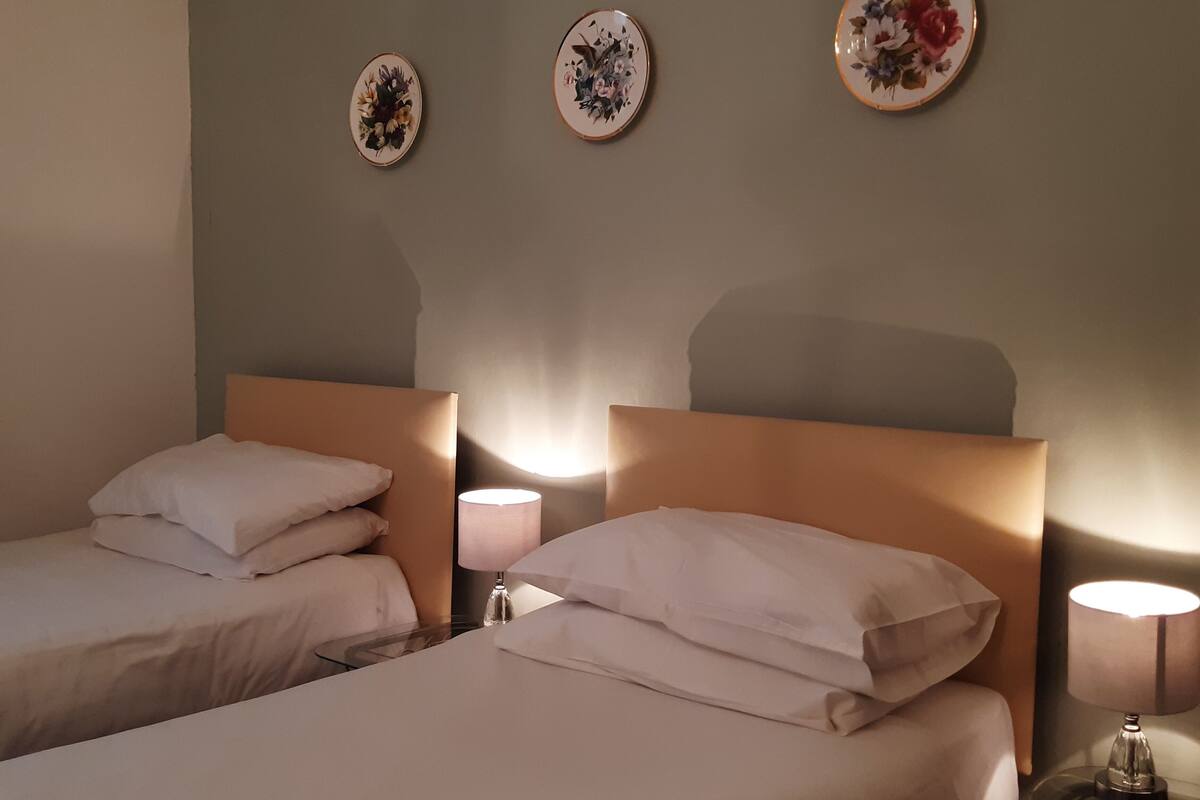 Een hotelkamer met twee bedden, elk voorzien van witte lakens en kussens, een tafeltje met een lamp, en drie decoratieve wandplaten.
