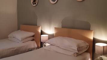 Habitación de hotel con dos camas, cada una con ropa blanca y almohadas, una mesita con lámpara y tres placas decorativas en la pared.