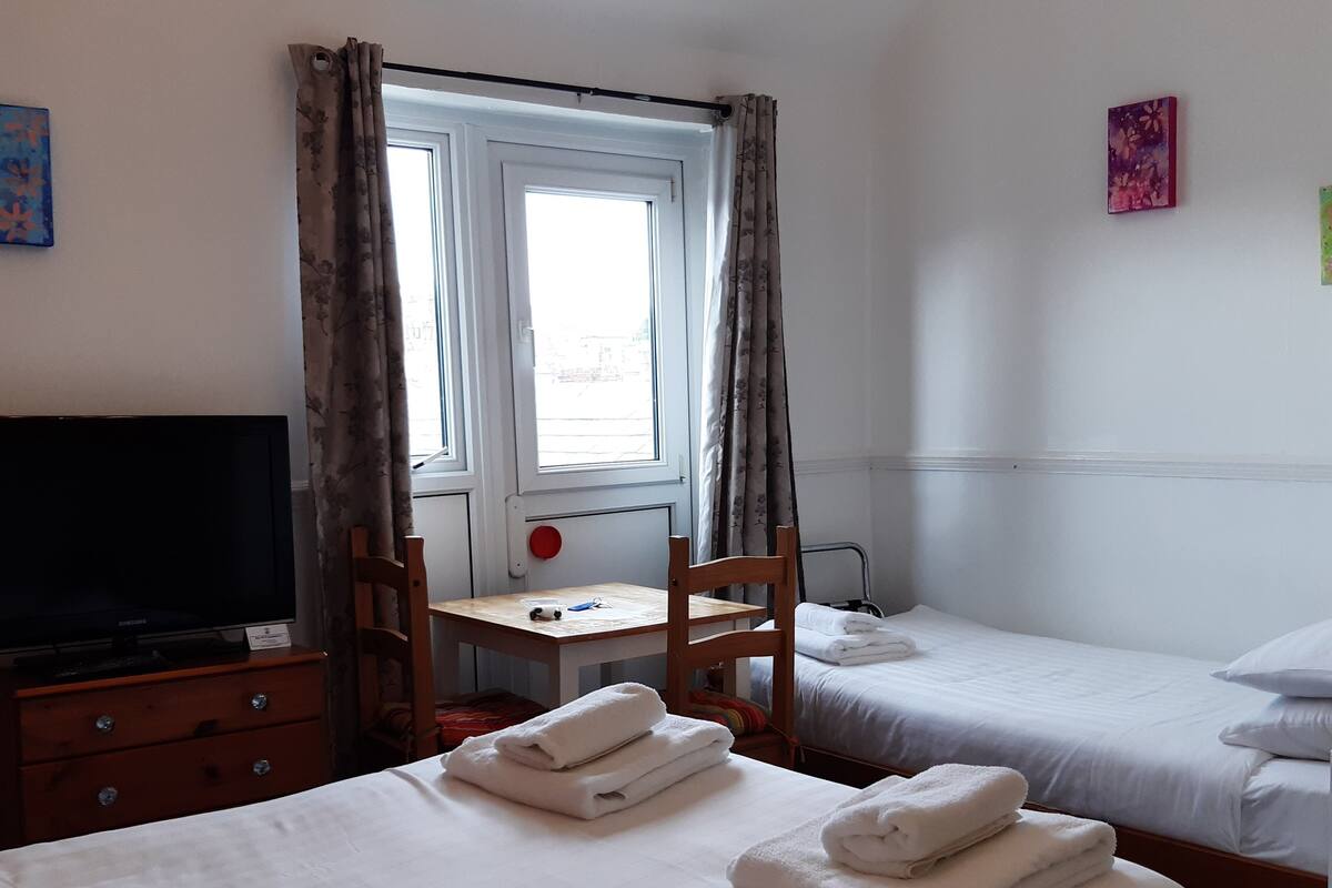 Een hotelkamer met twee bedden, een bureau, een televisie en een raam met gordijnen.