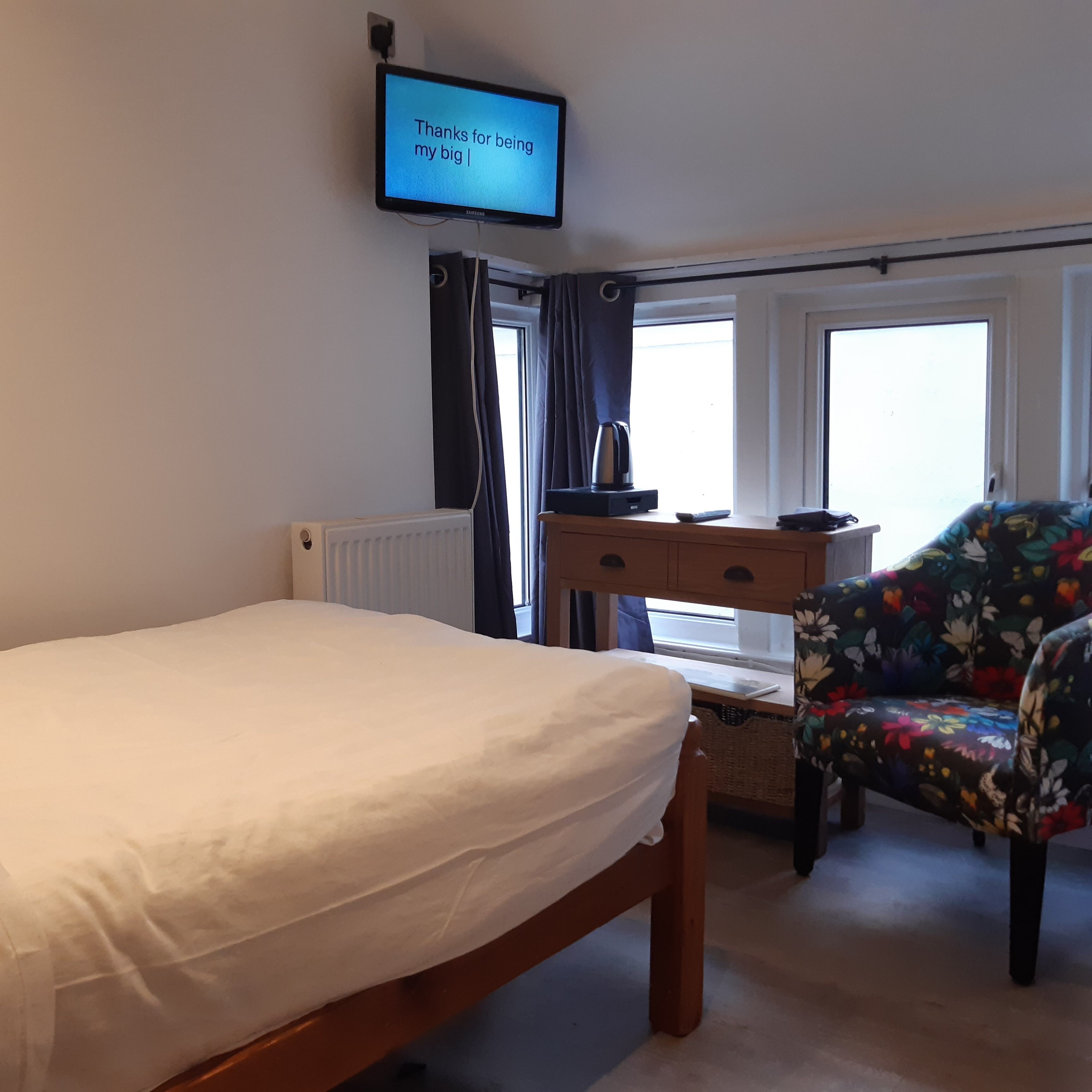 Ein Hotelzimmer mit einem Bett, einem Schreibtisch mit Computer, einem Sessel und einem Fernseher, der eine Meldung zeigt.