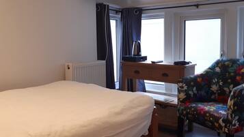 Ein Hotelzimmer mit einem Bett, einem Schreibtisch mit Computer, einem Sessel und einem Fernseher, der eine Meldung zeigt.