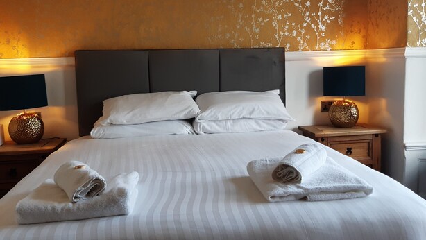 Ein Hotelzimmer mit einem großen Bett, zwei Nachttischen mit Lampen und einem blumigen Wanddesign.