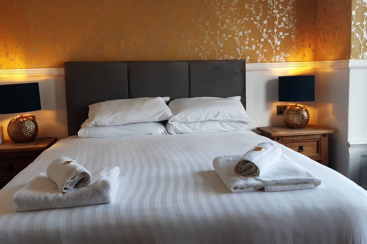 Een hotelkamer met een groot bed, twee nachtkastjes met lampen, en een behang met bloemenmotief.