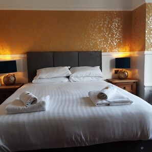 A hotel room with a large bed, two bedside tables with lamps, and a floral wallpaper design.