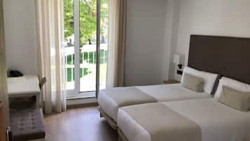Quarto de hotel com duas camas, uma escrivaninha e uma cadeira.