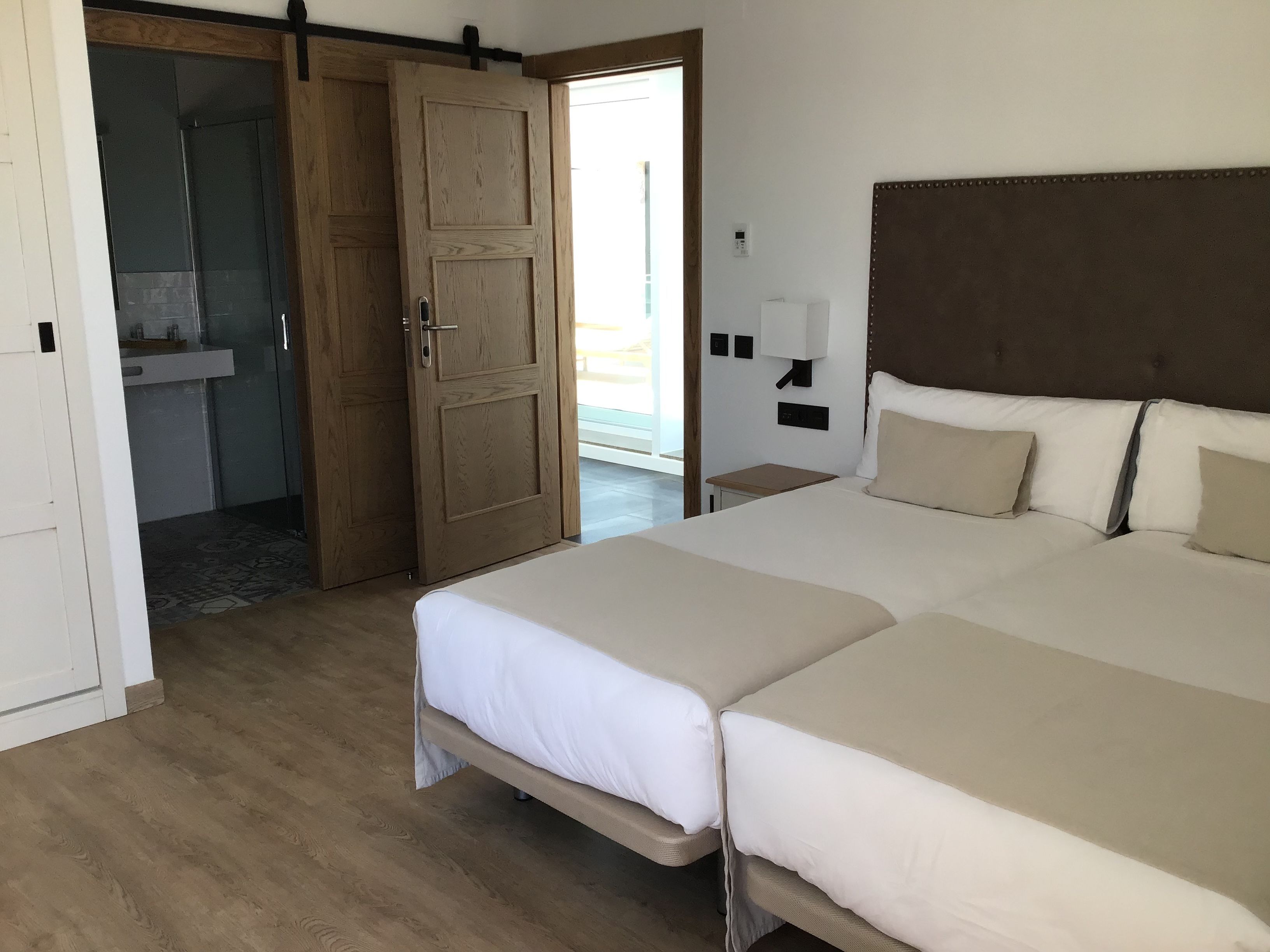A hotel room with a large bed, a wooden wardrobe, a bathroom with a sink, and a view of the outside.
