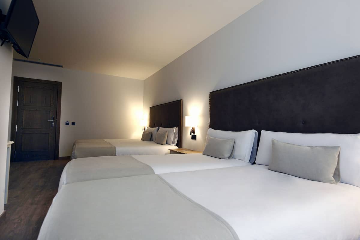 A hotel room with two beds, a dark headboard, bedside lamps, and a wooden door.