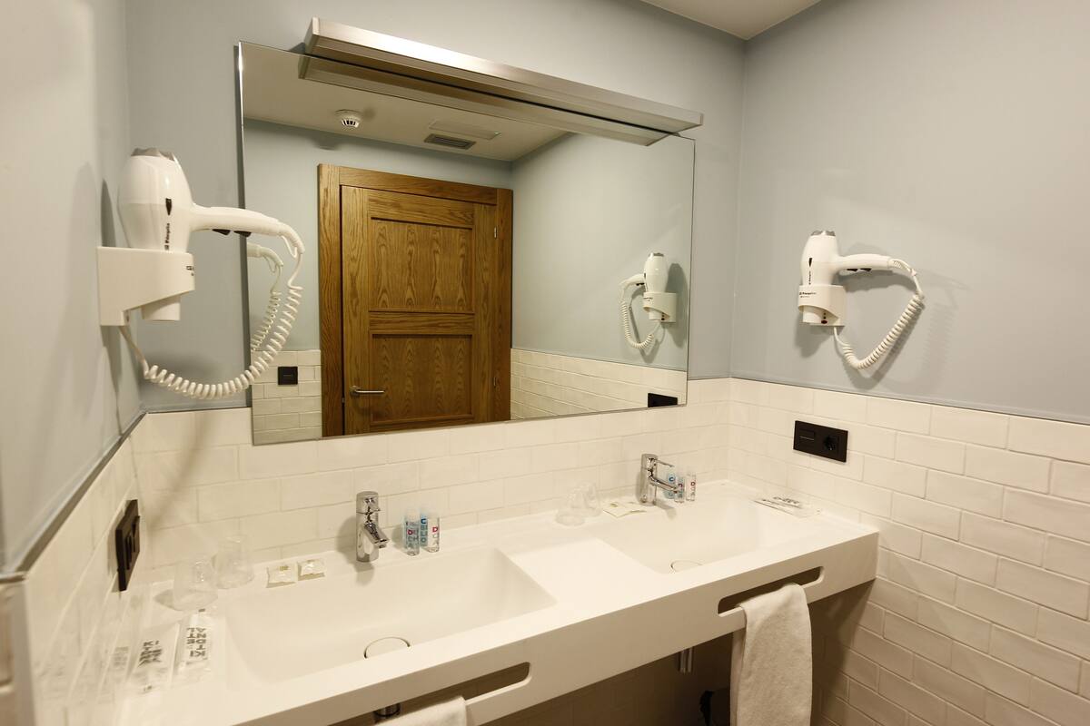 A bathroom with two sinks, a mirror, a hairdryer, and a towel rack.