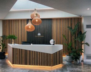 A hotel reception desk with a modern design, featuring a wooden panel backdrop, three hanging pendant lights, and a reception counter. - Hotel Vistalegre (Portomarin)